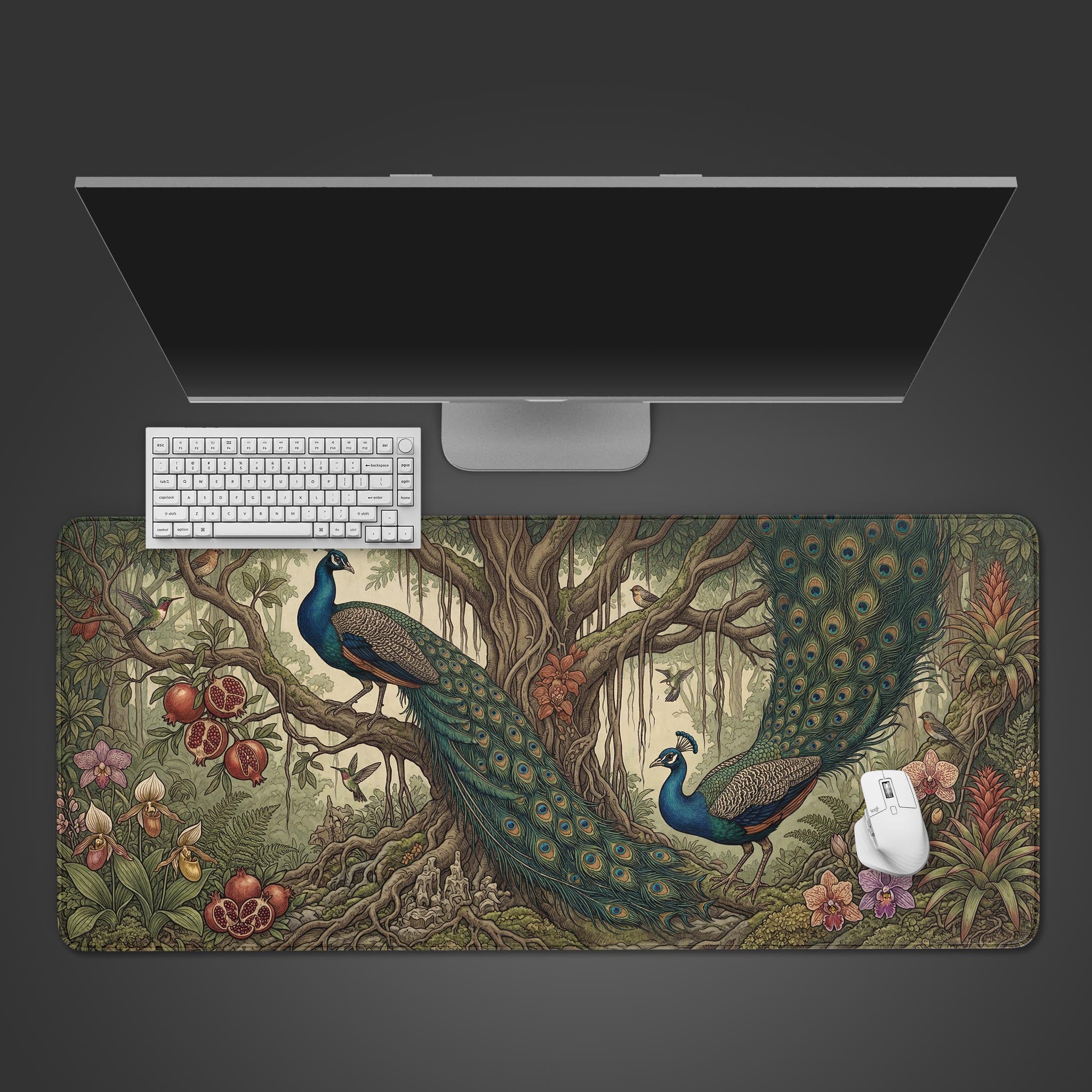 A wide desk mat featuring a vintage botanical illustration of two peacocks among ancient tree roots and pomegranates.