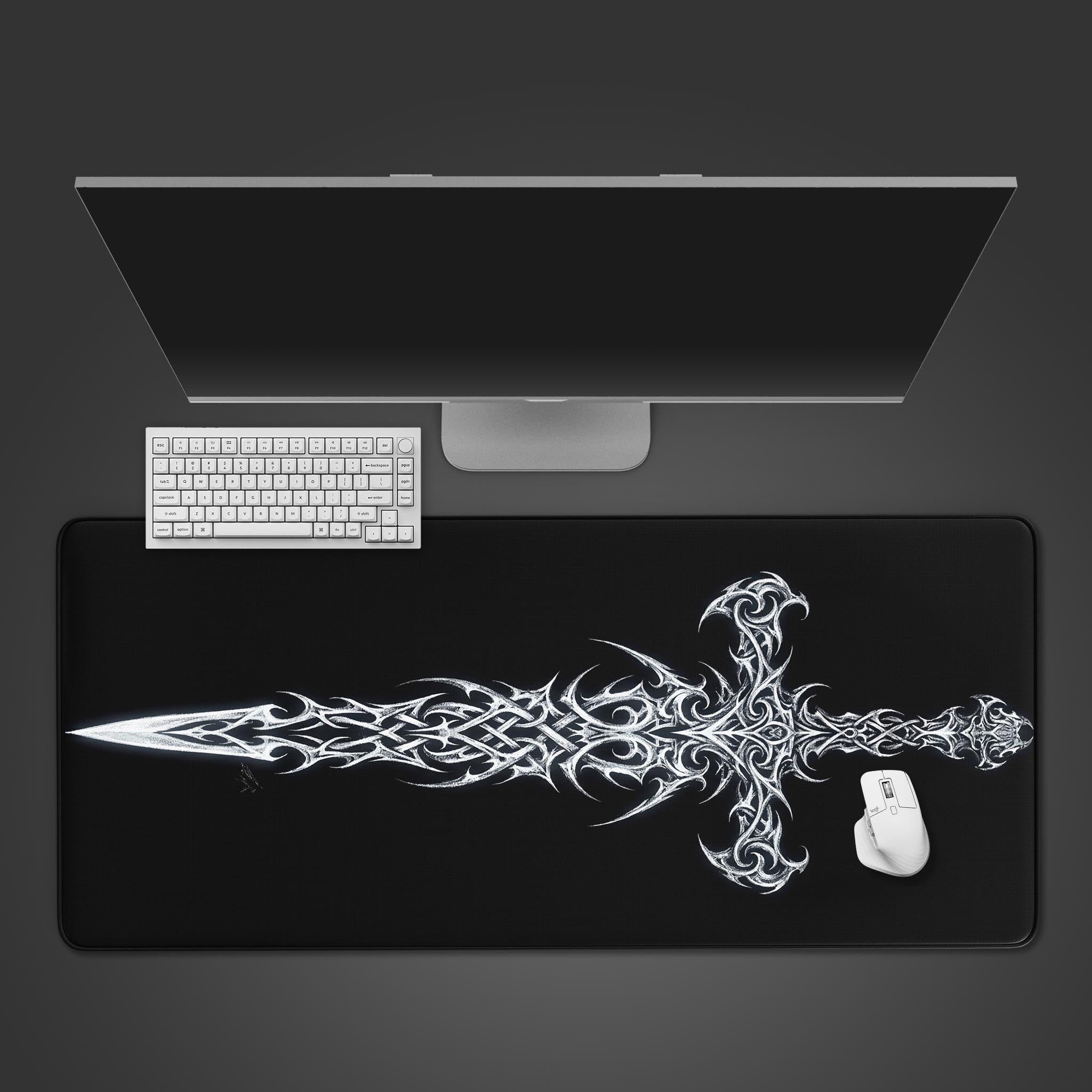 A top-down view of the Void Blade gaming desk mat, featuring a white tribal sword design. A white keyboard and mouse are positioned on the mat below a monitor. - Epic Design Pads & Mousepads