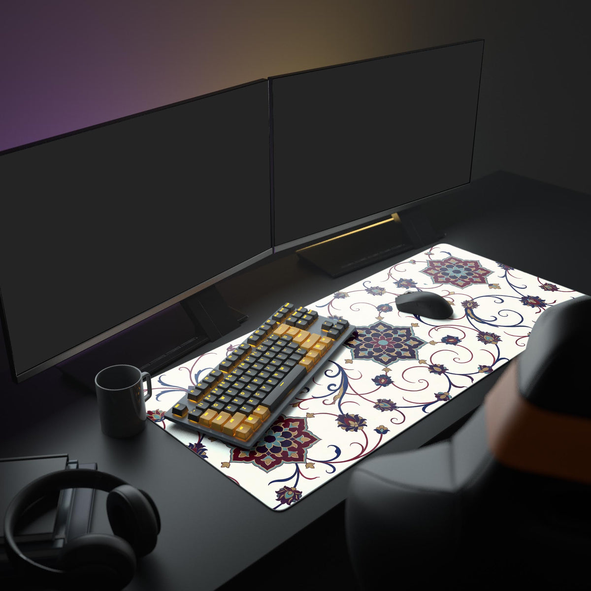 Ivory floral arabesque desk mat on a dark desk with dual monitors, a dark and amber keyboard, mouse, mug and headphones
