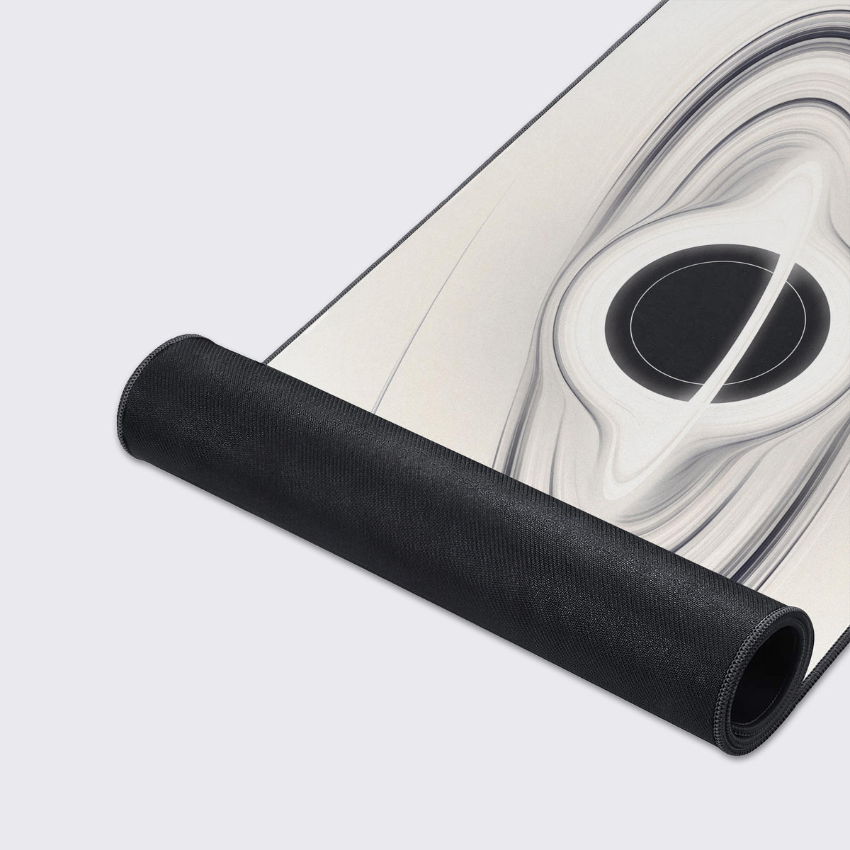 Ivory black hole desk mat partly rolled up, showing its black non-slip rubber underside below the swirling ring artwork