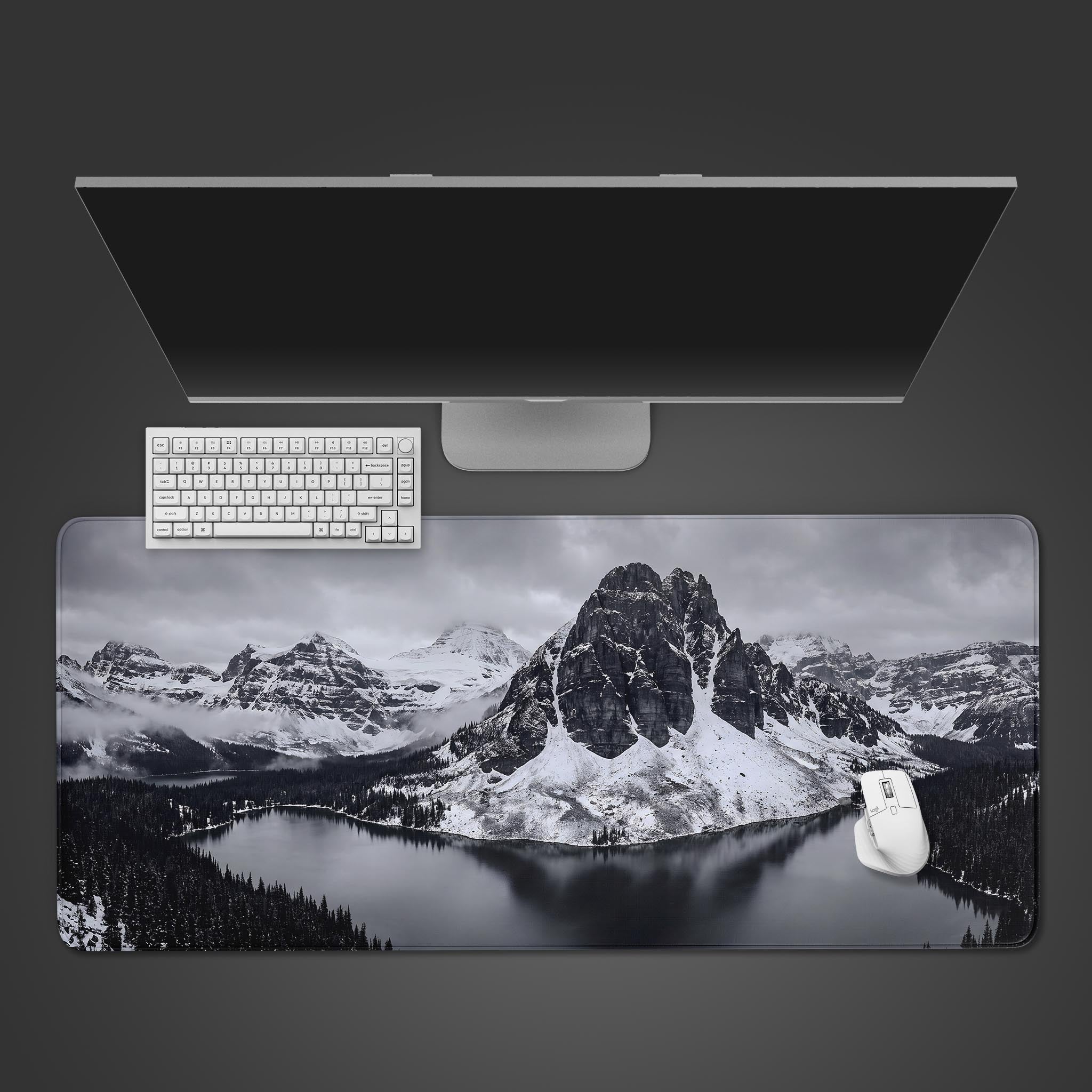 A black and white desk mat displaying a towering snow-covered mountain peak reflecting in a calm dark lake.