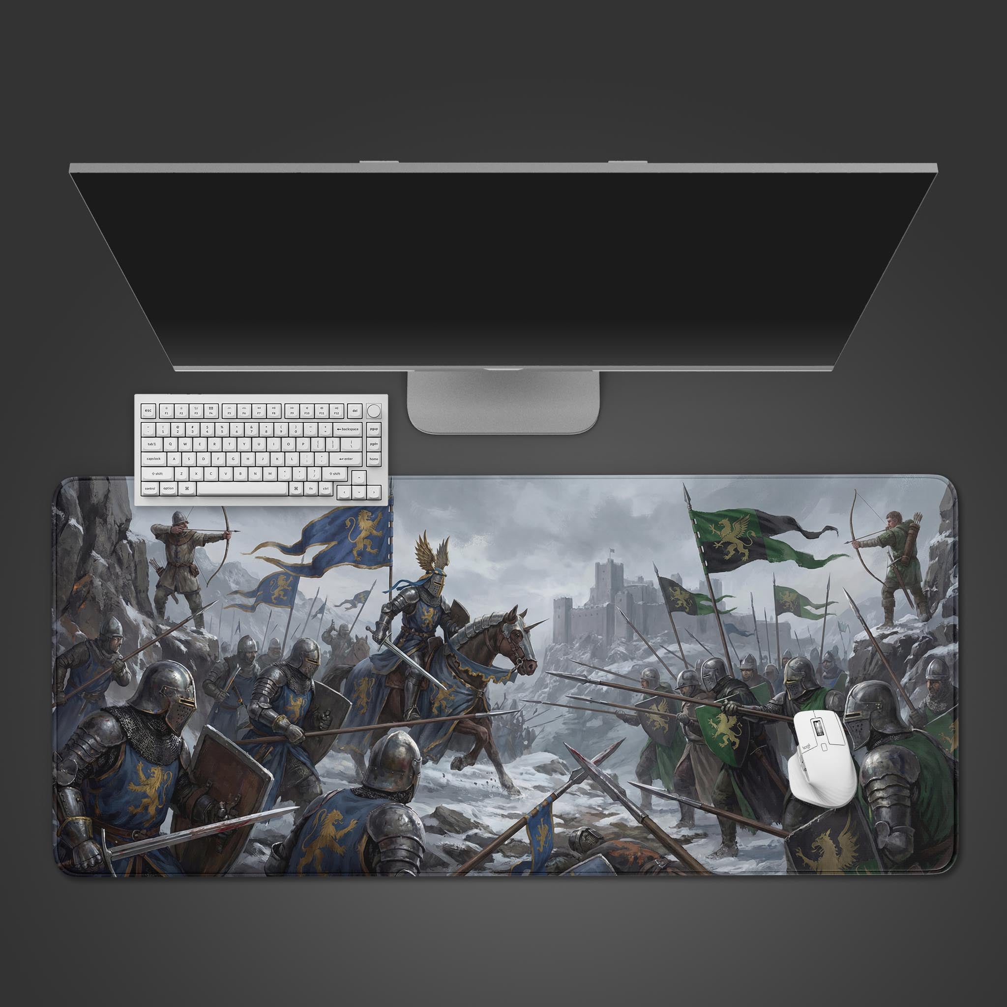 Top-down view of the Winter Siege gaming desk mat showing a medieval battle. A white keyboard and mouse are placed on the mat, below a large monitor on a gray background. - Epic Design Pads & Mousepads